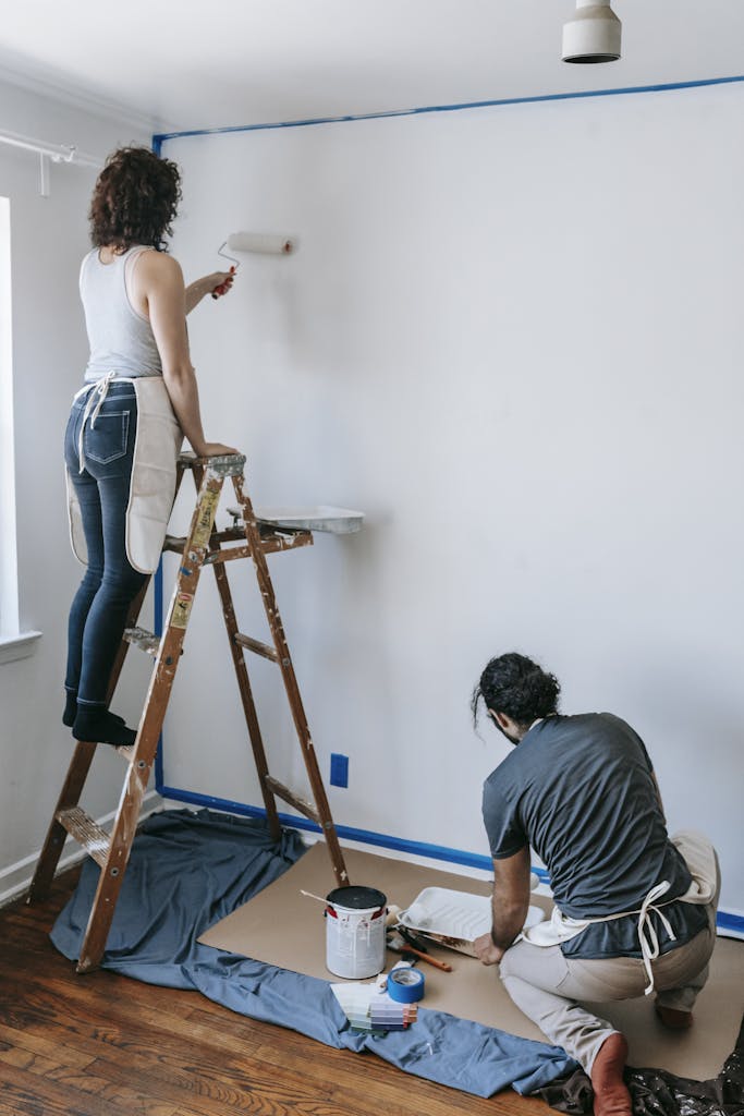 A couple working on a home renovation project, painting a room with rollers.