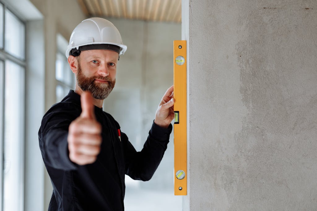 Professional construction worker with hard hat and spirit level giving thumbs up indoors.